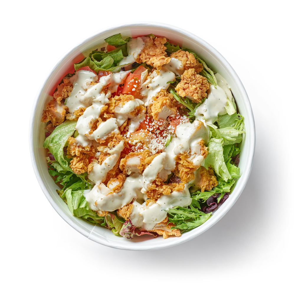 A salad featuring fried chicken and tomatoes, topped with Caesar dressing, like the fried chicken salad served at The Monroe, one of the best restaurants in Orlando for lunch.