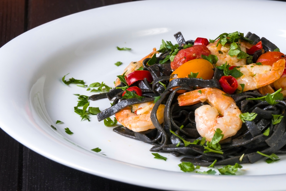 Black squid ink fettucine pasta is served with shrimp, cherry tomatoes, and garnish, like that served at Turchi Pasta, one of the best restaurants in Orlando for Italian food.