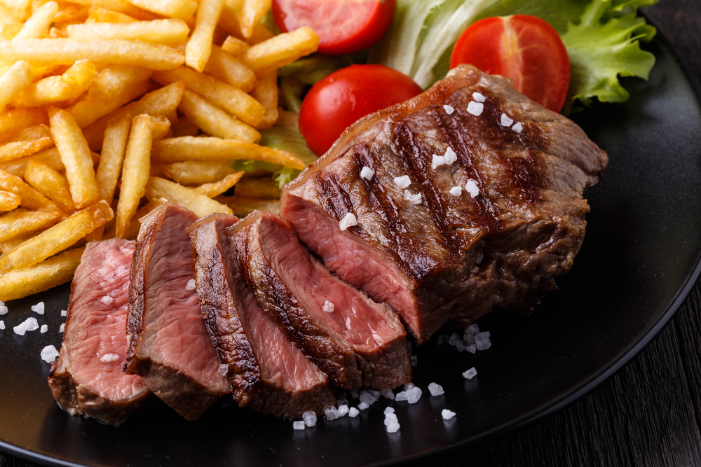 Slices of steak sit on a black plate with french fries and a cherry tomato, like the steak frites served at the Ravenous Pig, one of the best restaurants near Orlando.