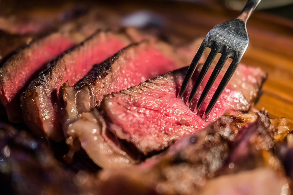 A close up of slices of rare cooked steak, with a fork in the foreground piece
