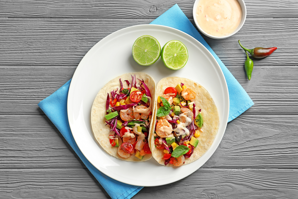 Two shrimp tacos filled with veggies sit on a white plate, with a blue napkin, like the tacos served at Reyes Mezcaleria, one of the best restaurants in Orlando for Mexican food.