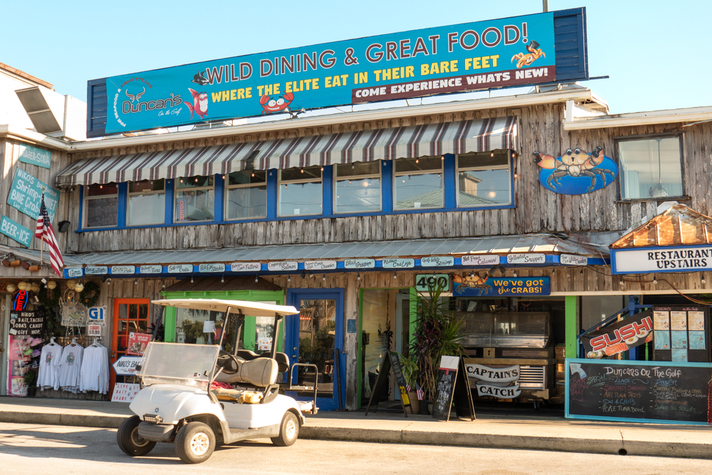 Colorful signs adorn a wooden shop building with a golf cart parked out front, in downtown Cedar Key, where walking around is one of the best things to do in Cedar Key.