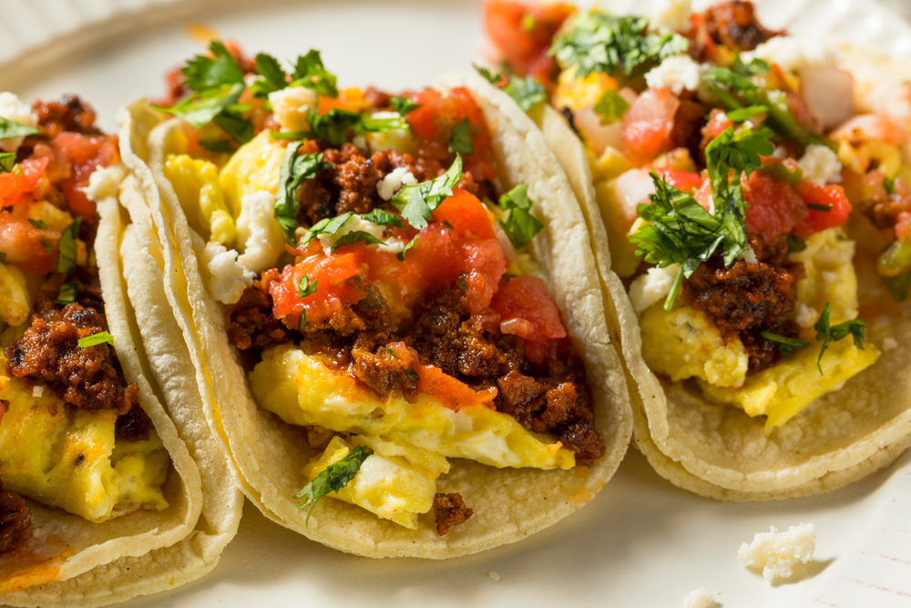 three mexician style tacos topped with salsa, eggs, ground beef and cheese