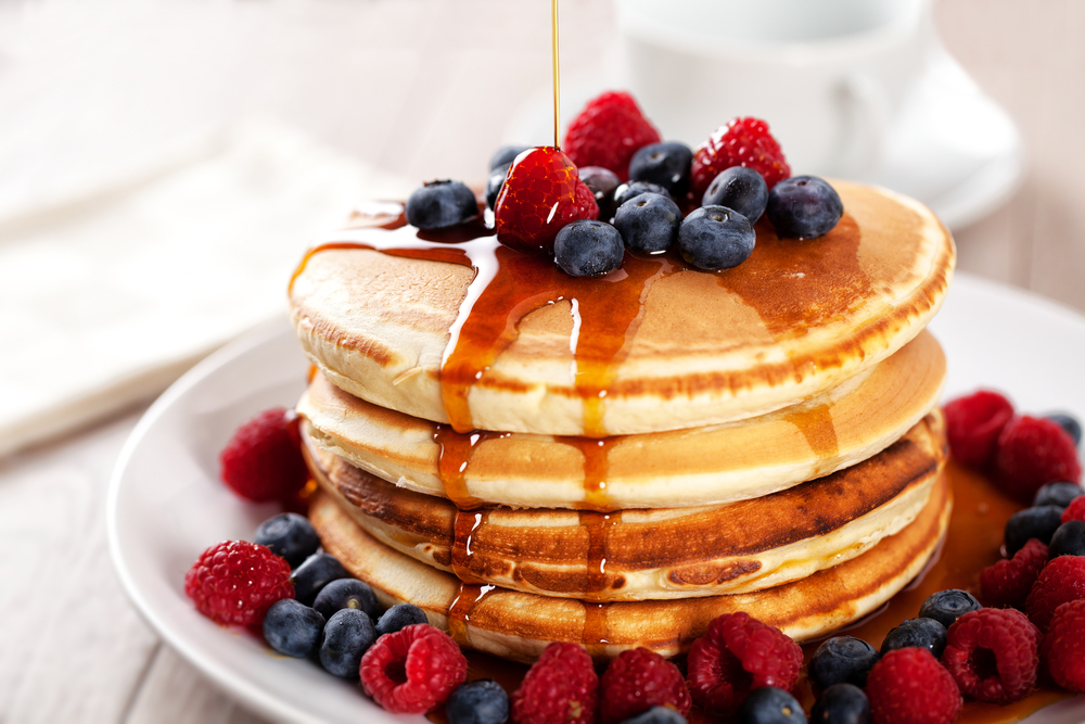 Fluffy tan stacked pancakes with berries on top, dripping with syrup.