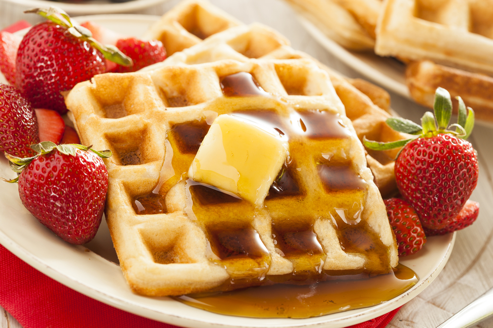 Waffles slathered in syrup and whole strawberries.