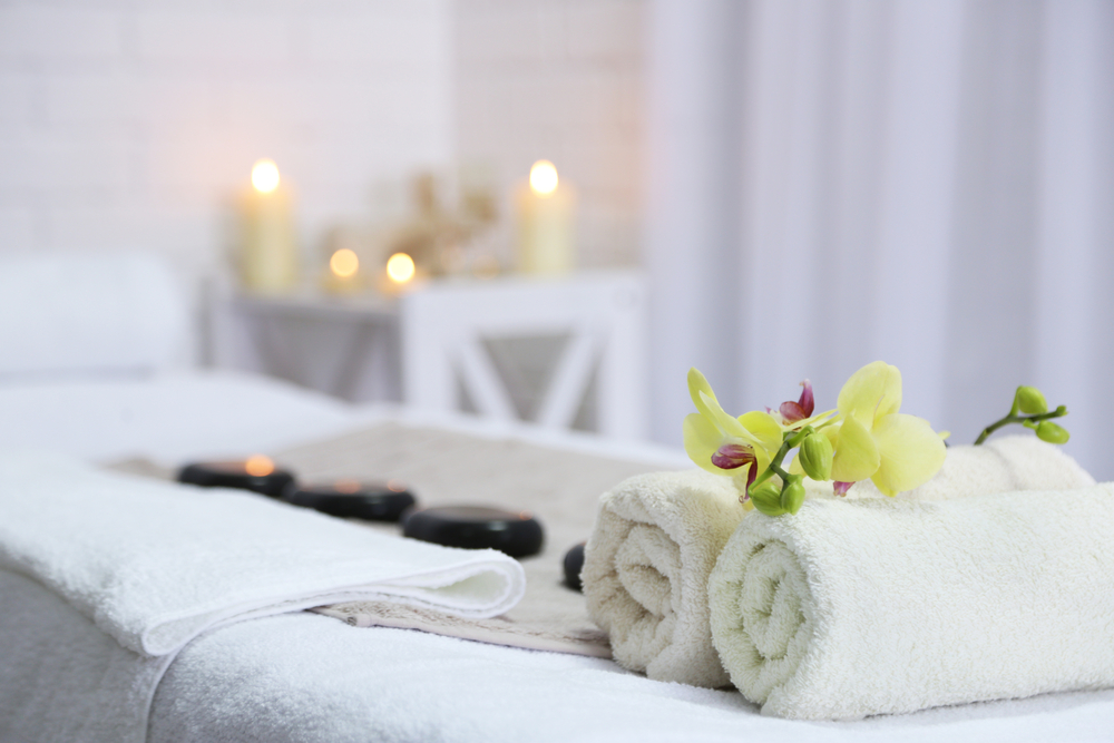 Towels, hot stones, and an orchid bloom sit on a massage table in a candle-lit spa.