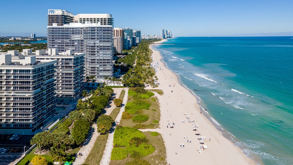 Blue waves wash upon Surfside Beach, with high rises stretching along the water on a sunny day.