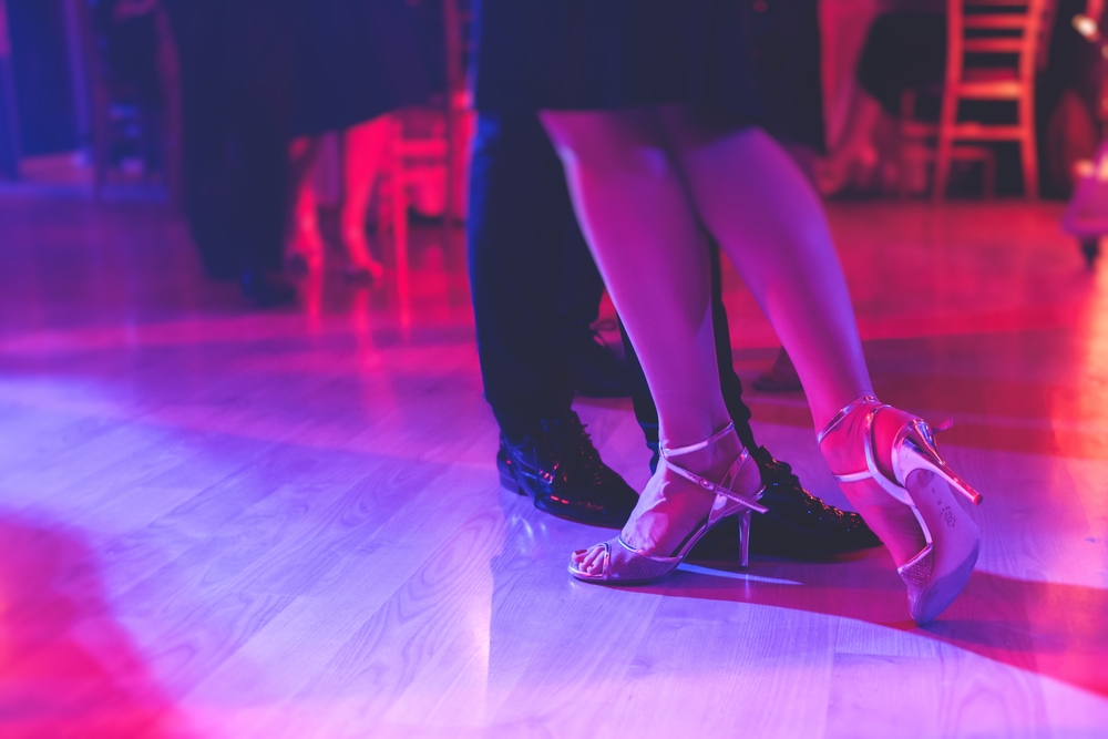 A man and woman's feet on a purple-hued dance floor while dancing salsa.