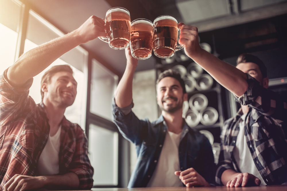 Three males cling their beer glasses together at a brewery, all in flannel shirts, enjoying Orlando for adults.