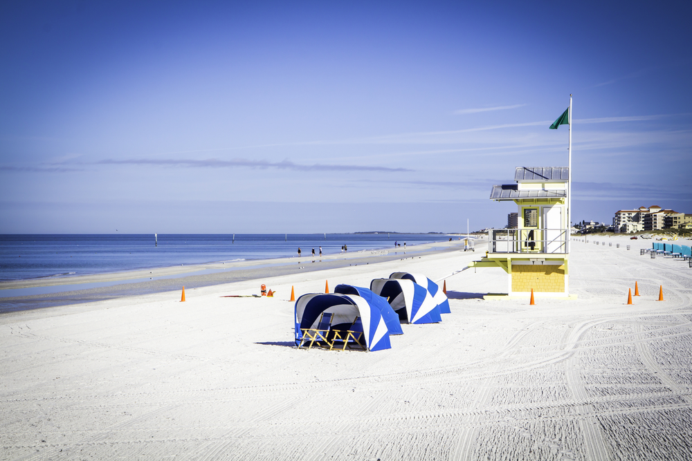 A beautiful morning on Clearwater Beach. The sky is blue and the sand is freshly raked. There is a lifeguard tower and some windbreaker tents. 