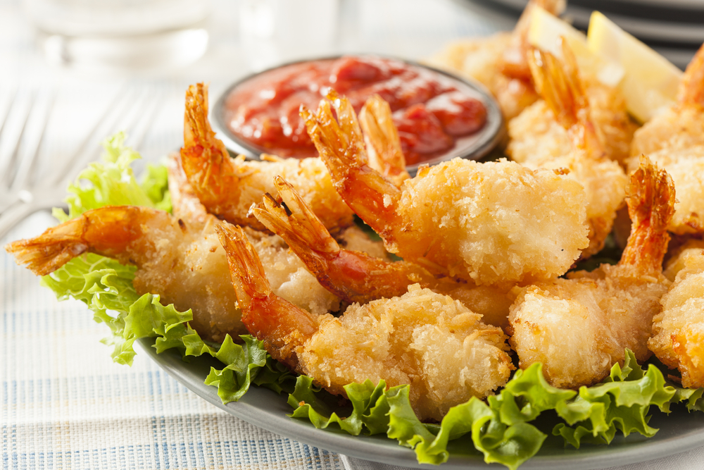 Fried coconut shrimp on a plate sitting on top of lettuce with red cocktail sauce on the side