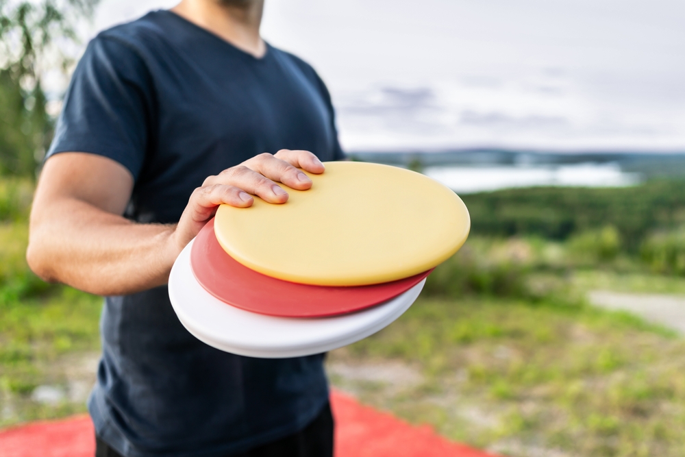 A man in a blue shirt holding three colorful throwing disks in a park ready to play disk golf