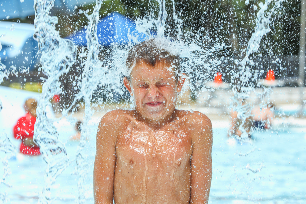 a young boy in a waterpark having fun while getting splashed by water above him