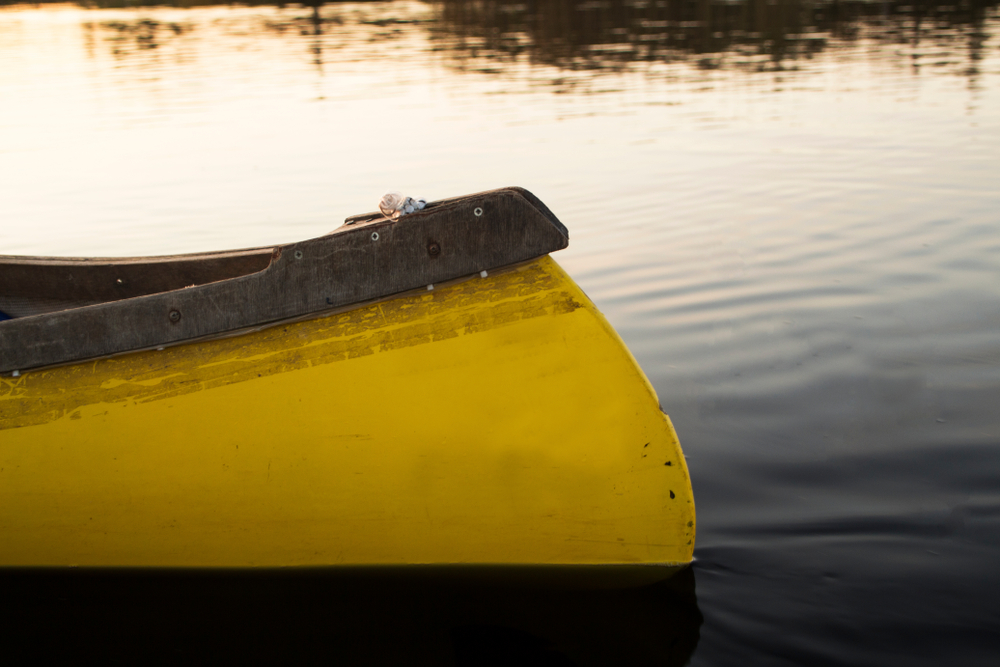 A close up shot of an old yellow kayak as it cuts through calm water.