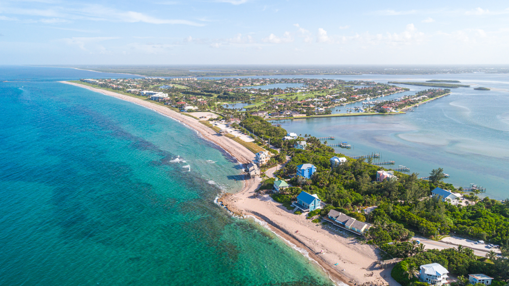 A bright aerial view of the city of Stuart Fl. Light blue sky, aqua blue ocean, sandy beach, and colorful buildings.