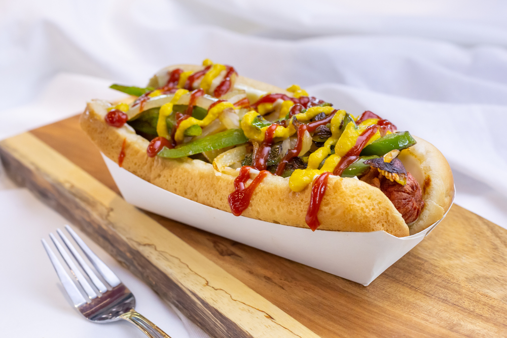 A loaded hot dog with extra onion, peppers, and condiments sits on a bun and is ready to eat! 