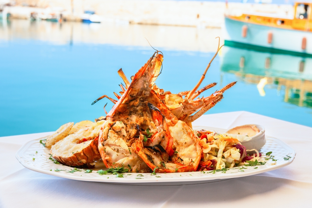 The lobster and crab plate in this photo is seasoned and featured with a butter dish as it sits on the cusp of a bar that looks out over the water.