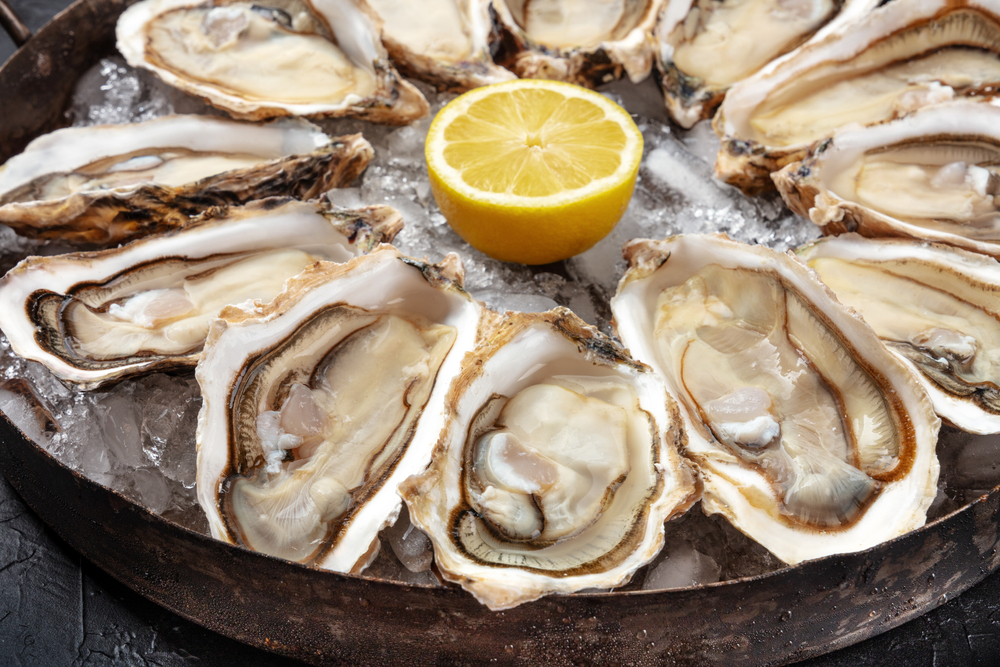 A collection of raw oysters sit on a bed of ice and a sliced lemon sits in the middle for this meal.