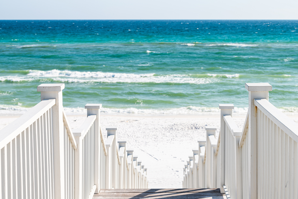 White staris leading down to a white beach and bright blue sea. 