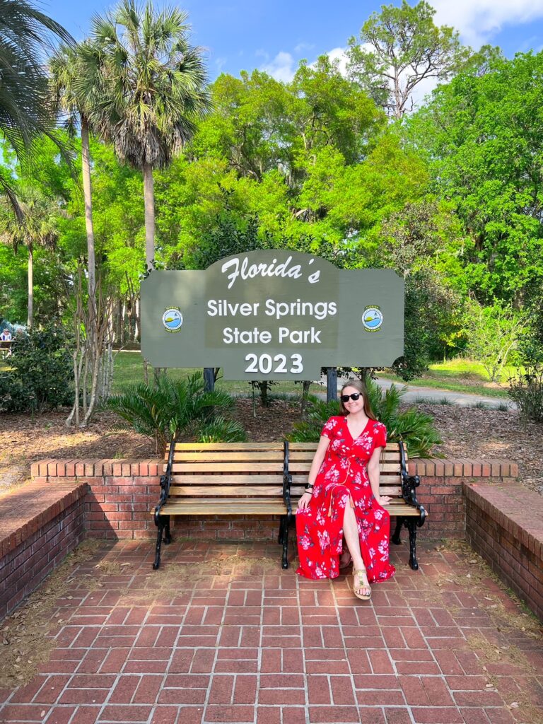 A womankind a red, floral dress and sunglasses sits at the Silver Springs State Park entrance in Florida. 