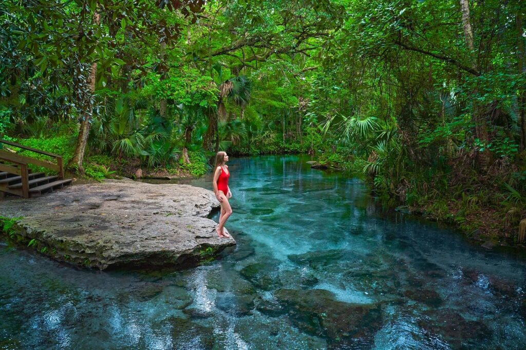 Woman in a red swimsuit standing on the edge of the blue water of Rock Springs.