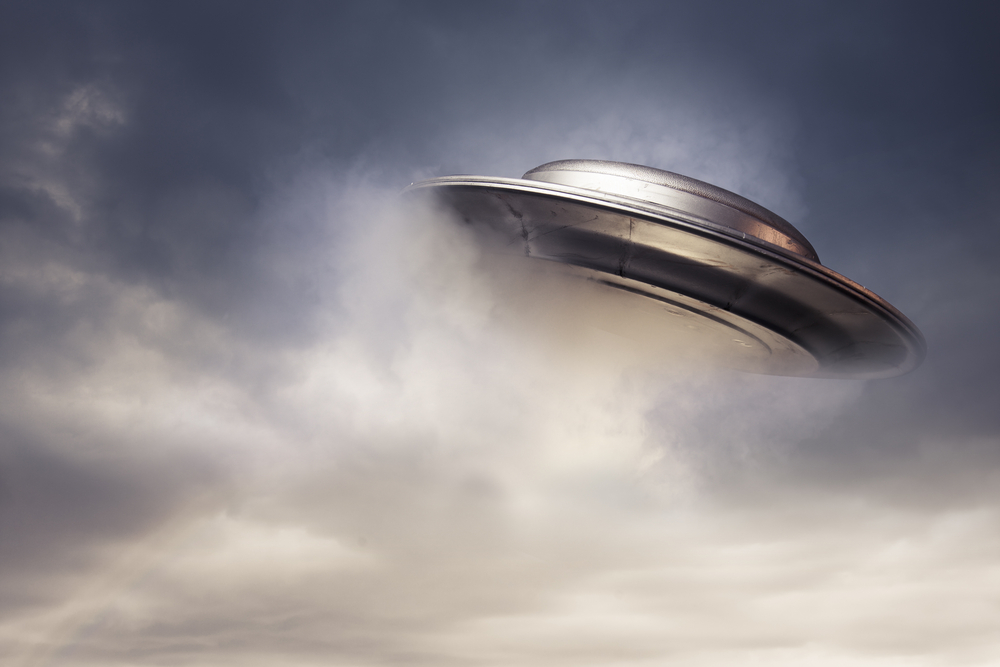 Metal UFO flying out of a cloud in a dark sky.