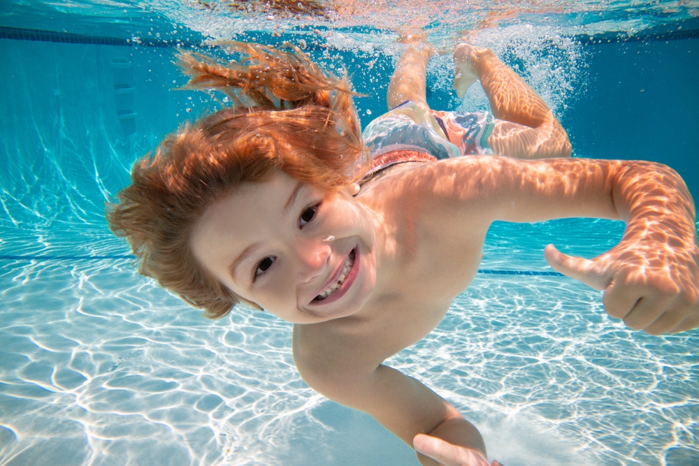 A young boy swimming underwater and smiling at the camera.