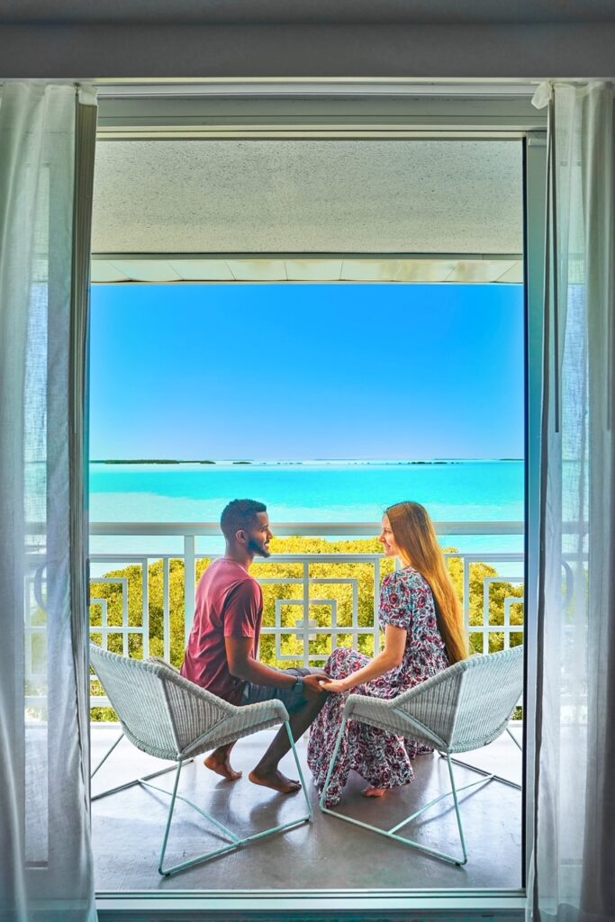 two people wearing the color red sitting on a hotel balcony overlooking the ocean