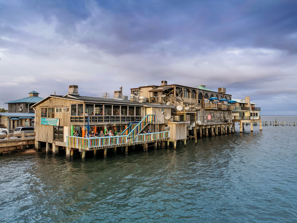 a bar/restaurant in the water on top of the ocean. there are colorful bars and umbrellas 