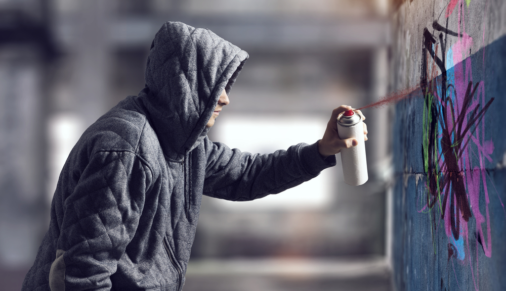 The crime rate in Florida is one of the cons of living in Florida: in this photo a man in a hoodie vandalizes public property, which is common in FL.