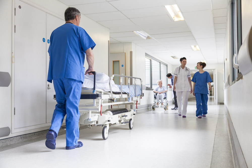 A nurse pushes a gurney down a hallway in a hospital while wearing blue scrubs. Florida's healthcare may be considered a con when considering moving here. 