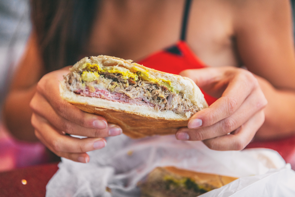A woman holds a cuban sandwich up close to the camera... food like this is found in Miami and is to die for! 