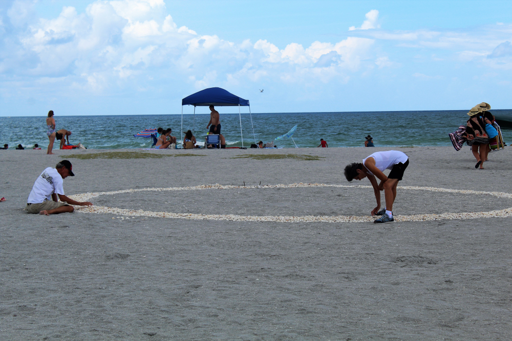 people at Venice beach looking through the sand with a blue tent and people enjoying the beach. 