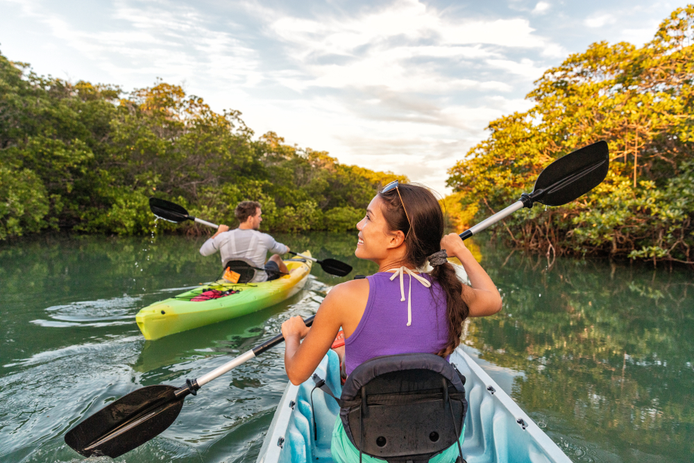 A man and woman kayaking on a sunny day down a river surrounded by trees best things to do in Venice Florida