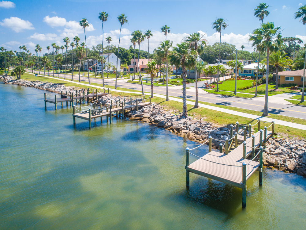 the beautiful docks on the side of the water in dunned florida. there are palm trees, clear waters, and homes right off the road. 