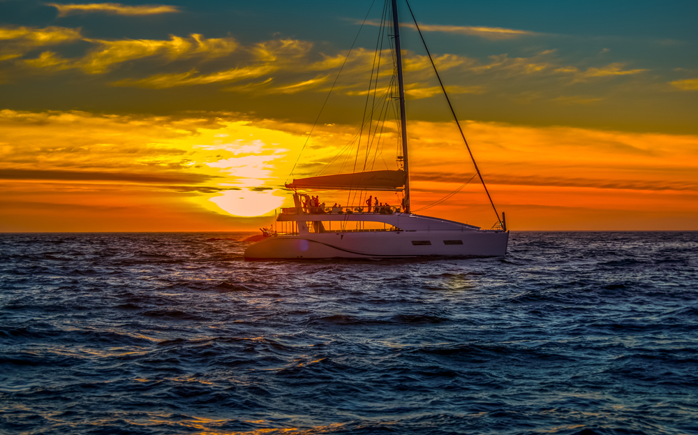 A sunset cruise takes guests across the deep blue sea while the sun dips beyond the horizon in dark hues of orange and yellow. 