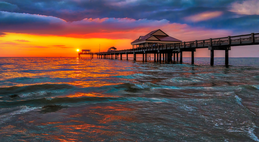 The orange sunset in Clearwater dips beyond the waves in the distance of Pier 60.