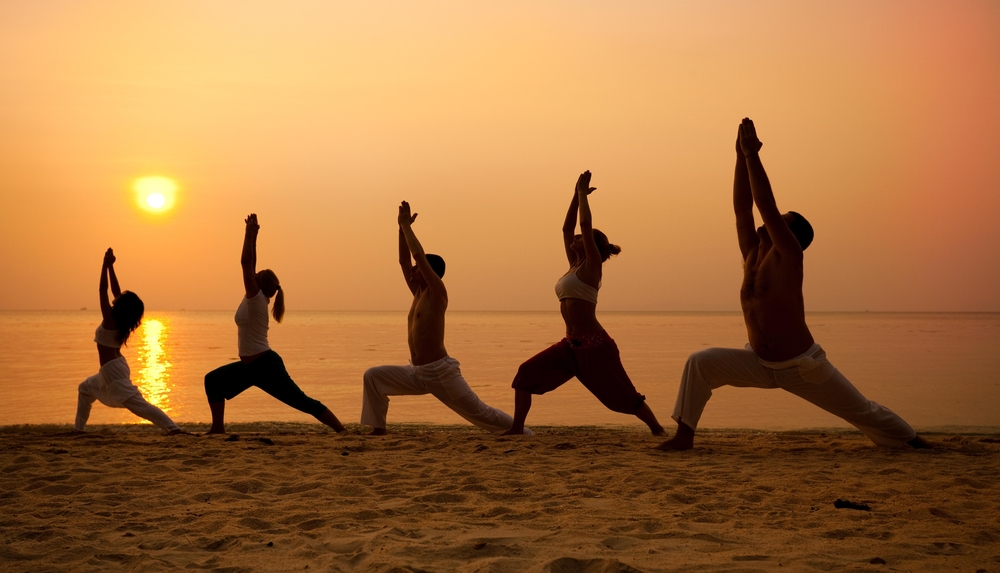 Five individuals pose in the sunset for a lesson of yoga as they truly relax. 