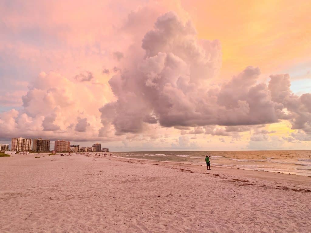 Big, puffy clouds are a strong contrast to the orange and yellow sky above Sand Key. 