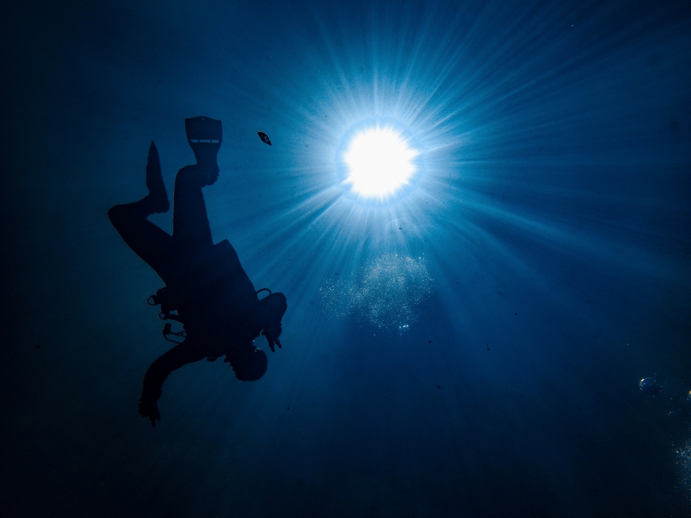 bright sunlight through dark exposure with a scuba diver continuing to descend in the water