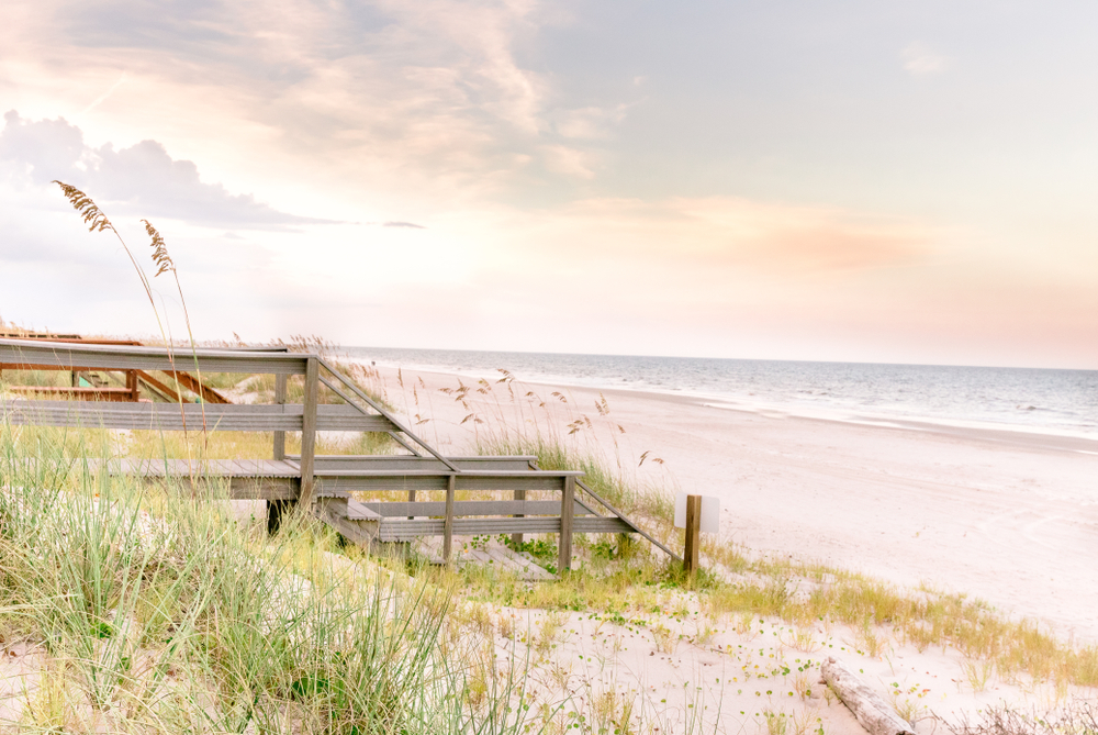 A soft sunrise touches the white sand of Amelia Island, as wooden stairs transcend onto the land.