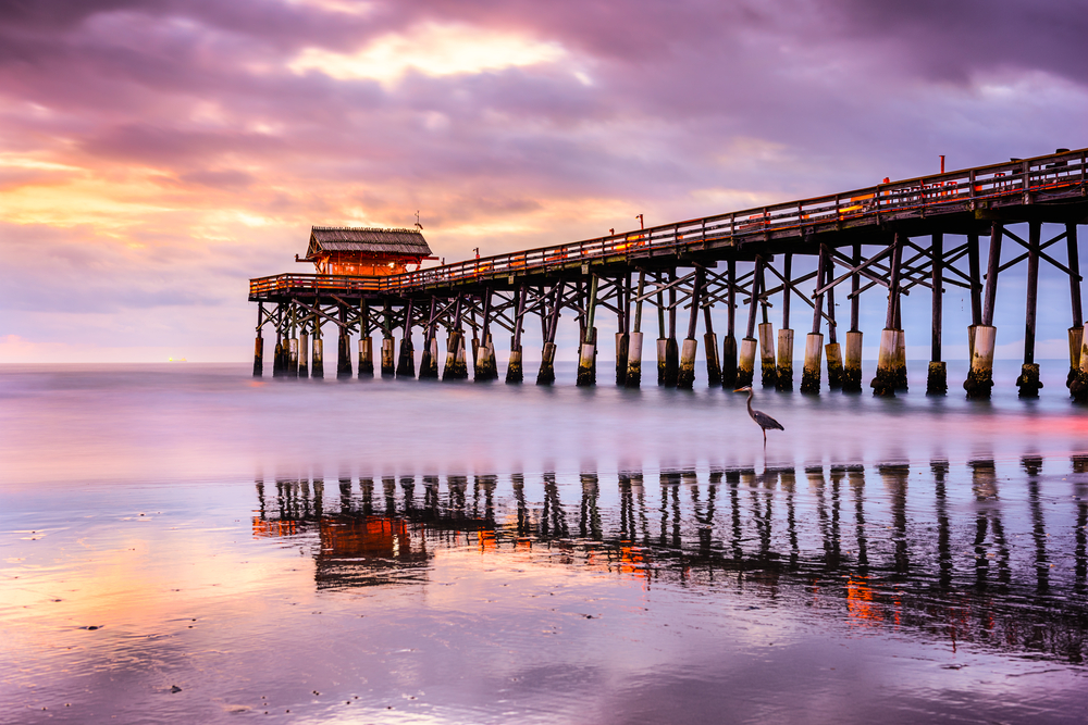 During one of the stunning sunsets in Florida, particularly in Cocoa Beach, a pier is set aglow in oranges as the water and sky give a purple light. 