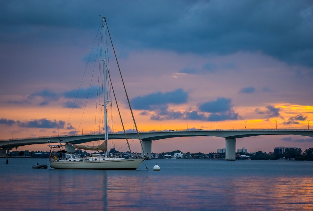 Sunset sky behind the John Ringling Causeway Bridge over Sarasota Bay. There is a boat in front of the bridge.