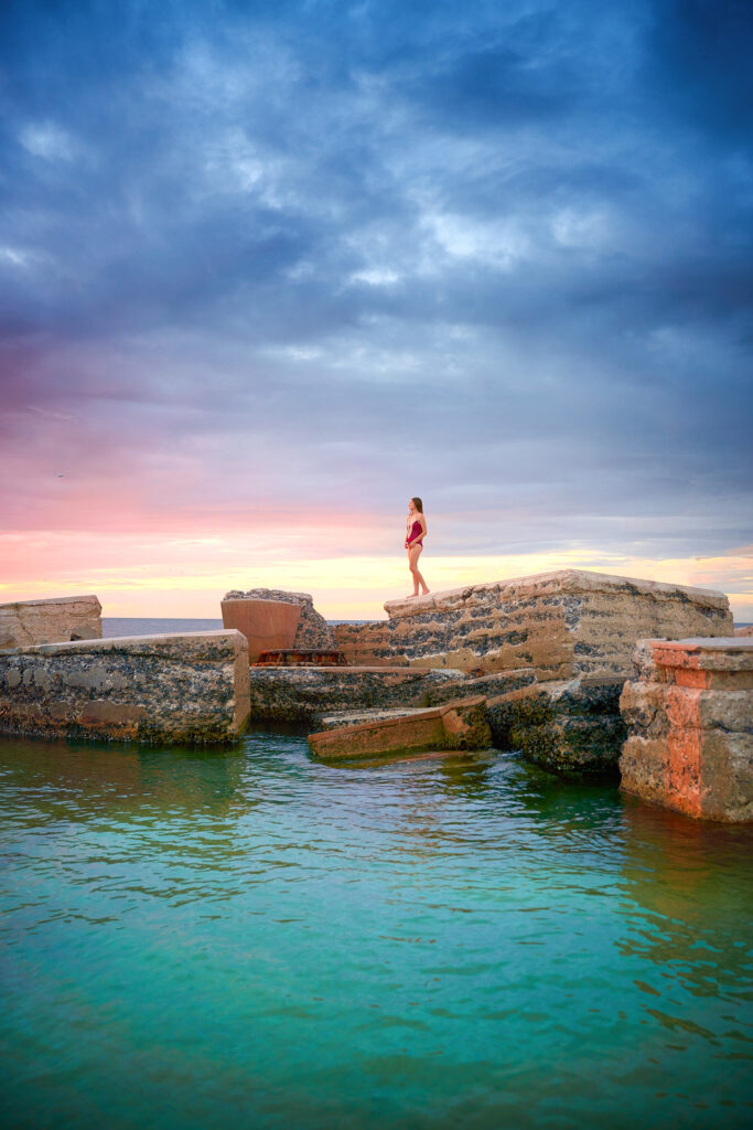A girl in a red bathing suit stands upon an abandoned fort to get a better view at the sky while enjoying sunsets in Florida. 