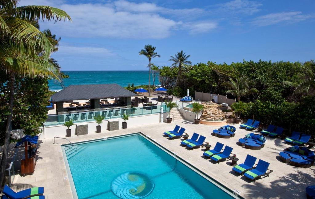 swimming pool at a hotel resort surrounded by greenery with the beach and ocean visible. 