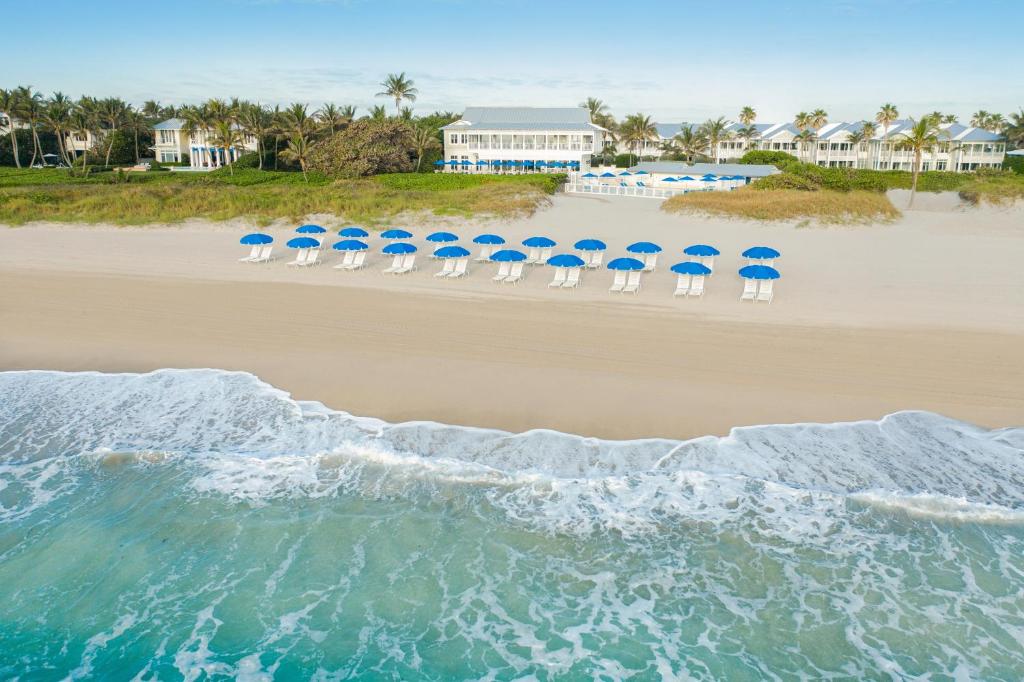 Private beach with white loungers and but umberellas in front of a white colonial style hotel. 