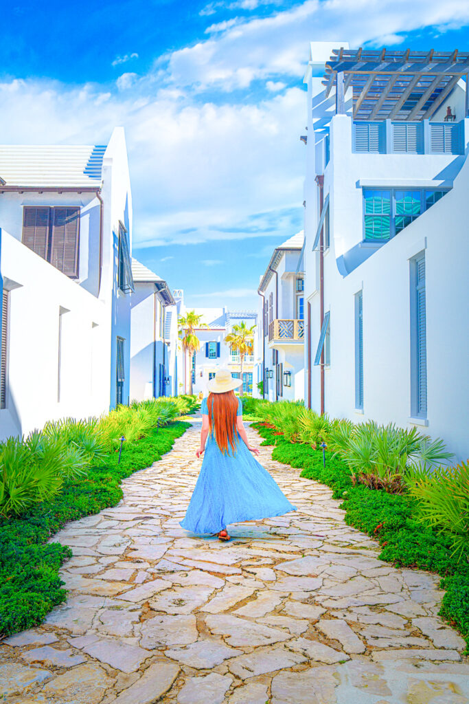 On your 30A travel guide a girl in value dress strolling down cobblestone streets surrounded by white buildings in Alys Beach