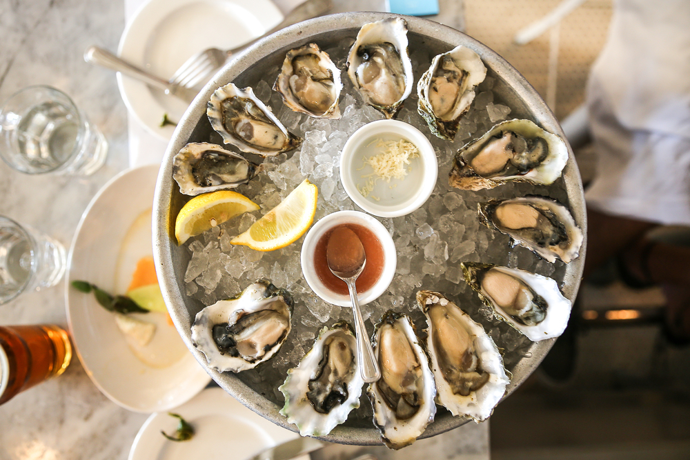 a plate of oysters on ice with lemon and sauce sitting on a table