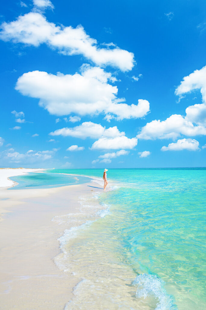 a girl in a white swimsuit standing in the turquoise water and white sand beaches without crowds along 30A