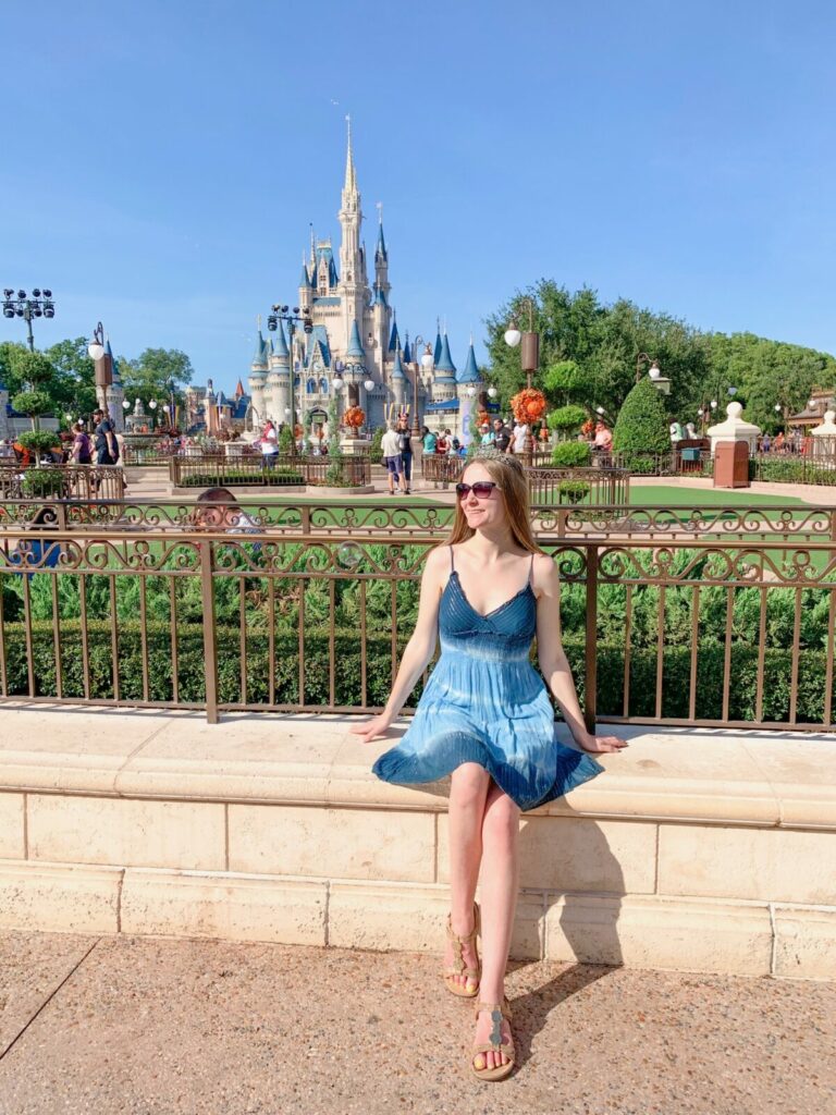 A women n a blue dress and crown sits in front of the old-school Cinderella castle at Magic Kingdom-- the colors aren't pink but blue! 